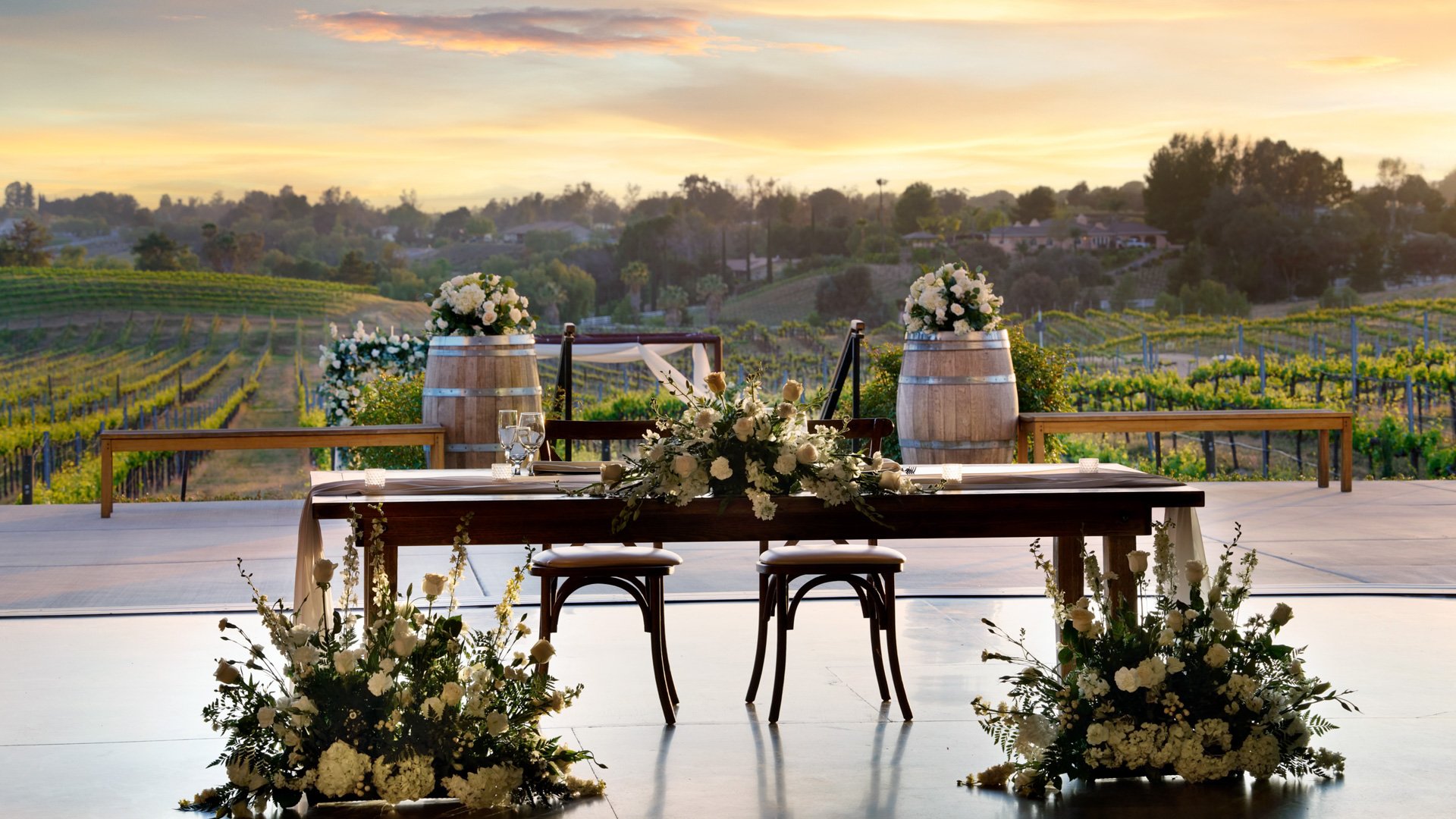 Sweetheart wedding table with white floral arrangements at Danza del Sol Winery in Temecula, CA, overlooking vineyard views at golden hour.