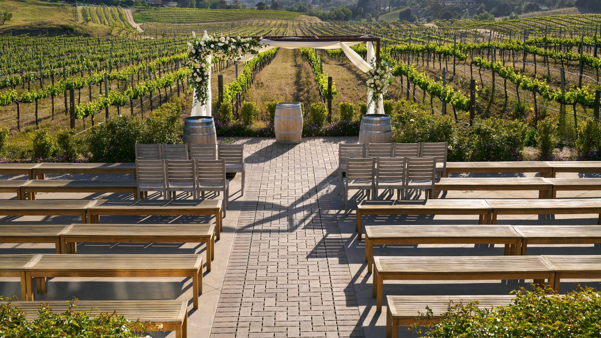 Wedding ceremony setup with wine barrel accents and floral archway in the vineyard at Danza del Sol Winery, Temecula, California.