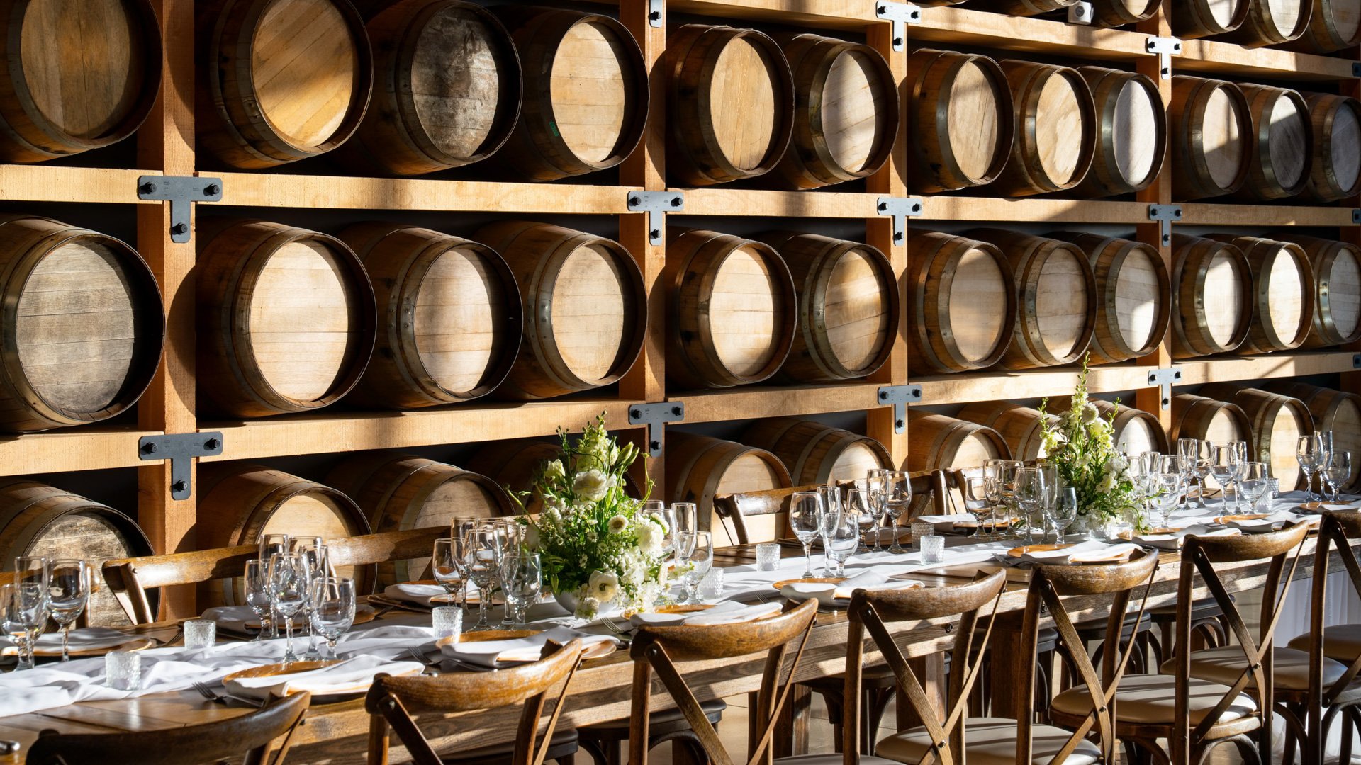 Close-up of winery wedding reception in the Barrel Room at Danza del Sol Winery in Temecula, featuring wine barrels, farmhouse tables, and floral centerpieces.