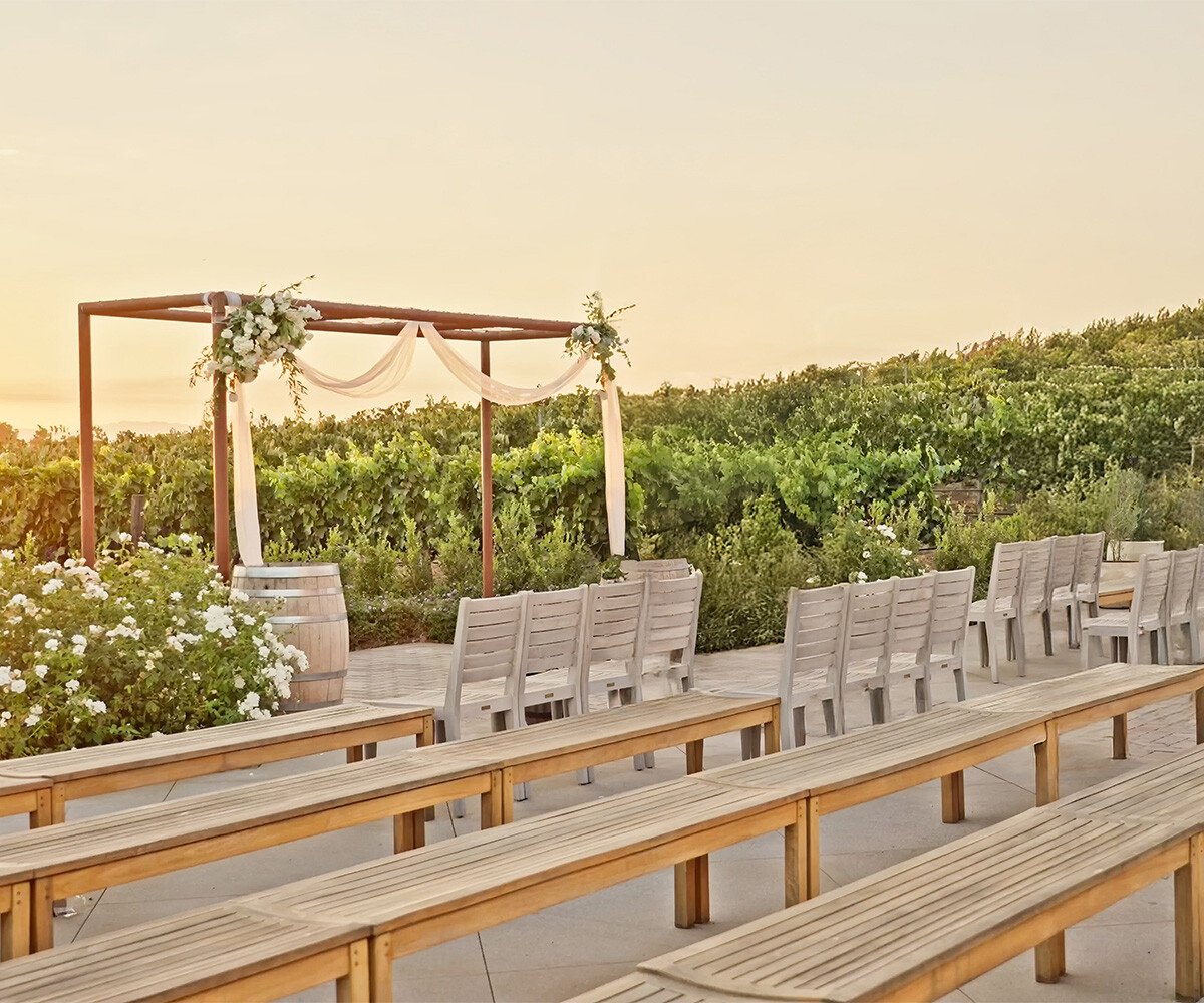 Sunset ceremony setup at Danza del Sol Winery featuring wooden benches, rustic pergola, and golden vineyard backdrop in Temecula.