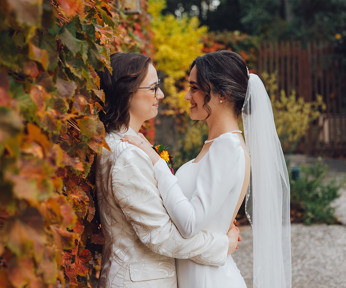 Two brides posing in front of ivy wall with autumn leaves - Hacienda de las Flores by Wedgewood Weddings