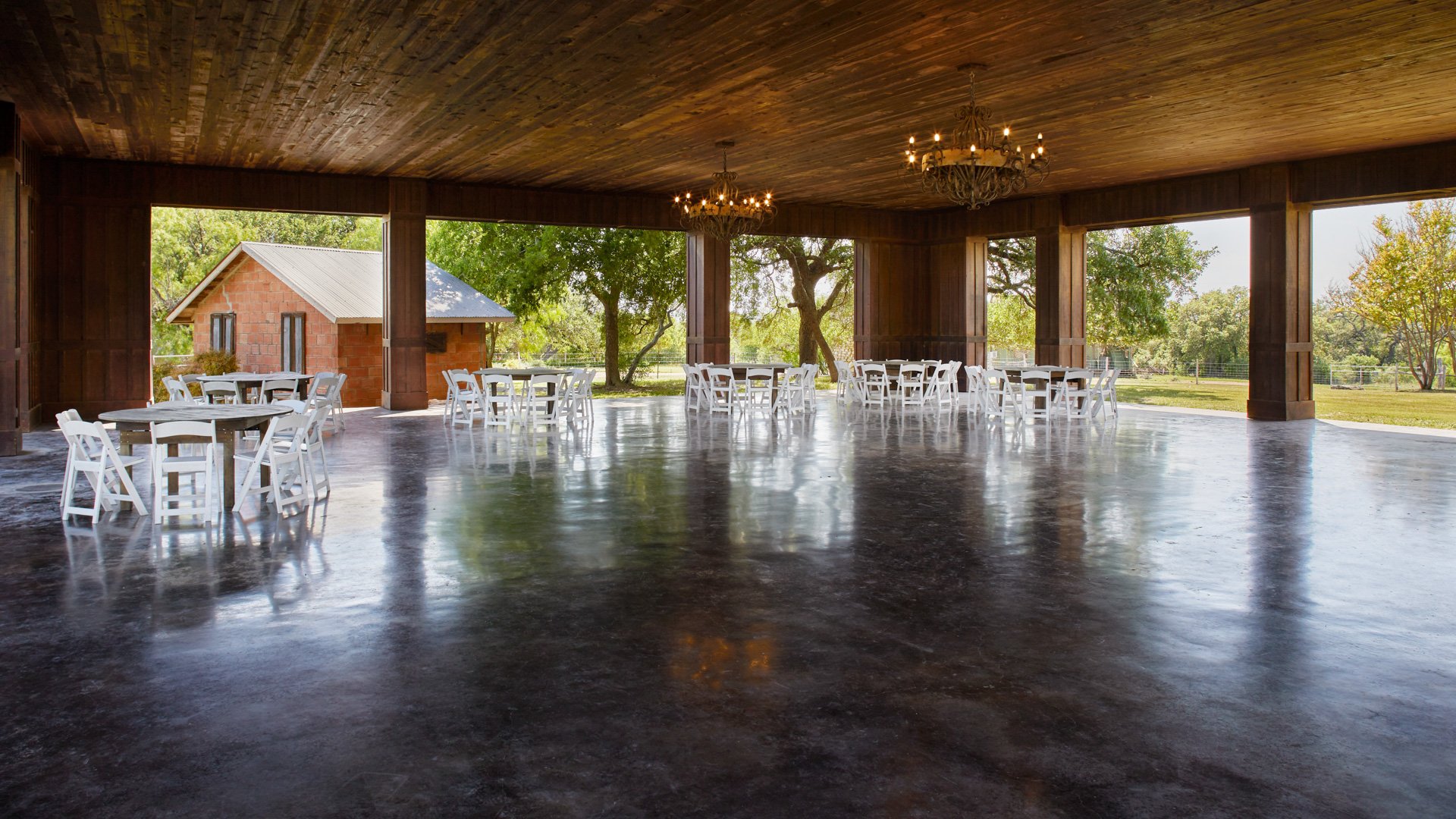 Open-air wedding reception at the Meadow Pavilion, Hofmann Ranch, with round tables, white linens, chandeliers, and countryside views.