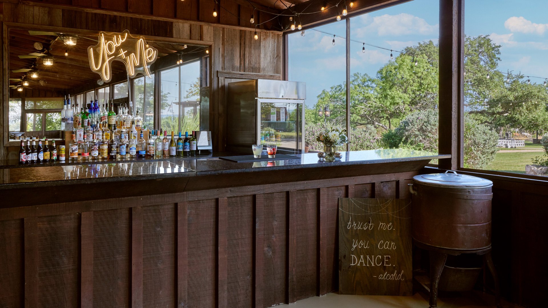 Rustic covered porch bar area at Hofmann Ranch set for cocktail hour, with string lights, wooden details, and full bar setup.