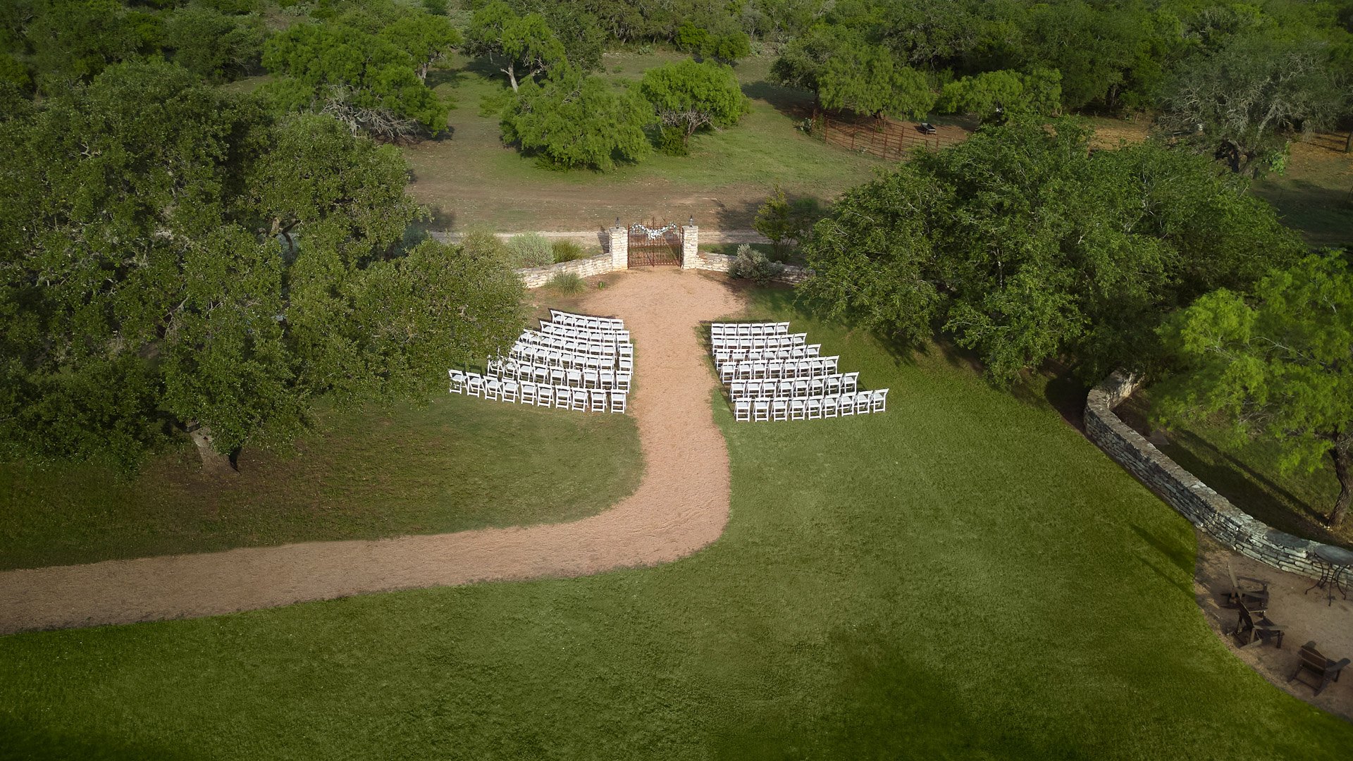 Drone view of the Iron Gate ceremony site at Hofmann Ranch, showcasing outdoor seating, stone walls, and Texas hill country landscape.