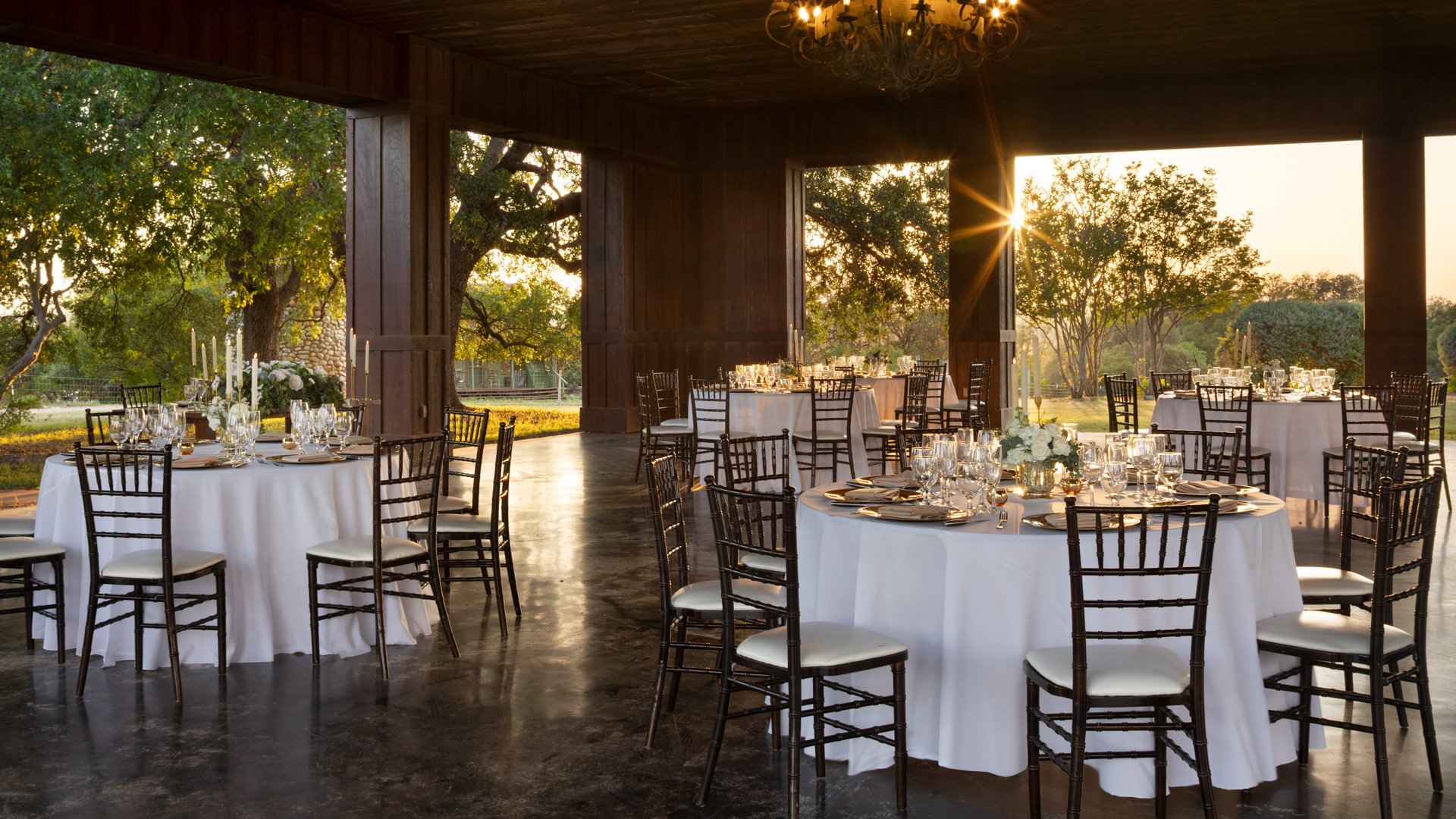 Meadow Pavilion wedding reception setup with elegant table settings, black chairs, and countryside views during golden hour.