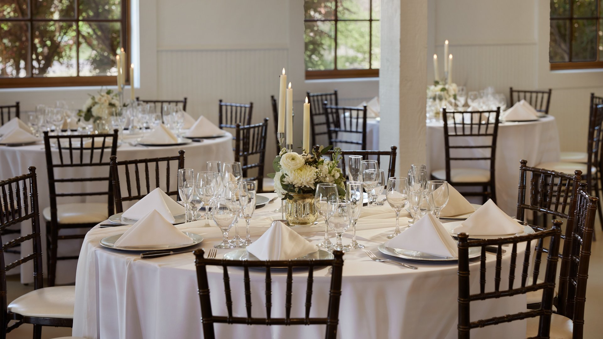Close-up of reception table at Hofmann Ranch Grande Hall with white linens, floral centerpiece, glassware, and glowing taper candles.