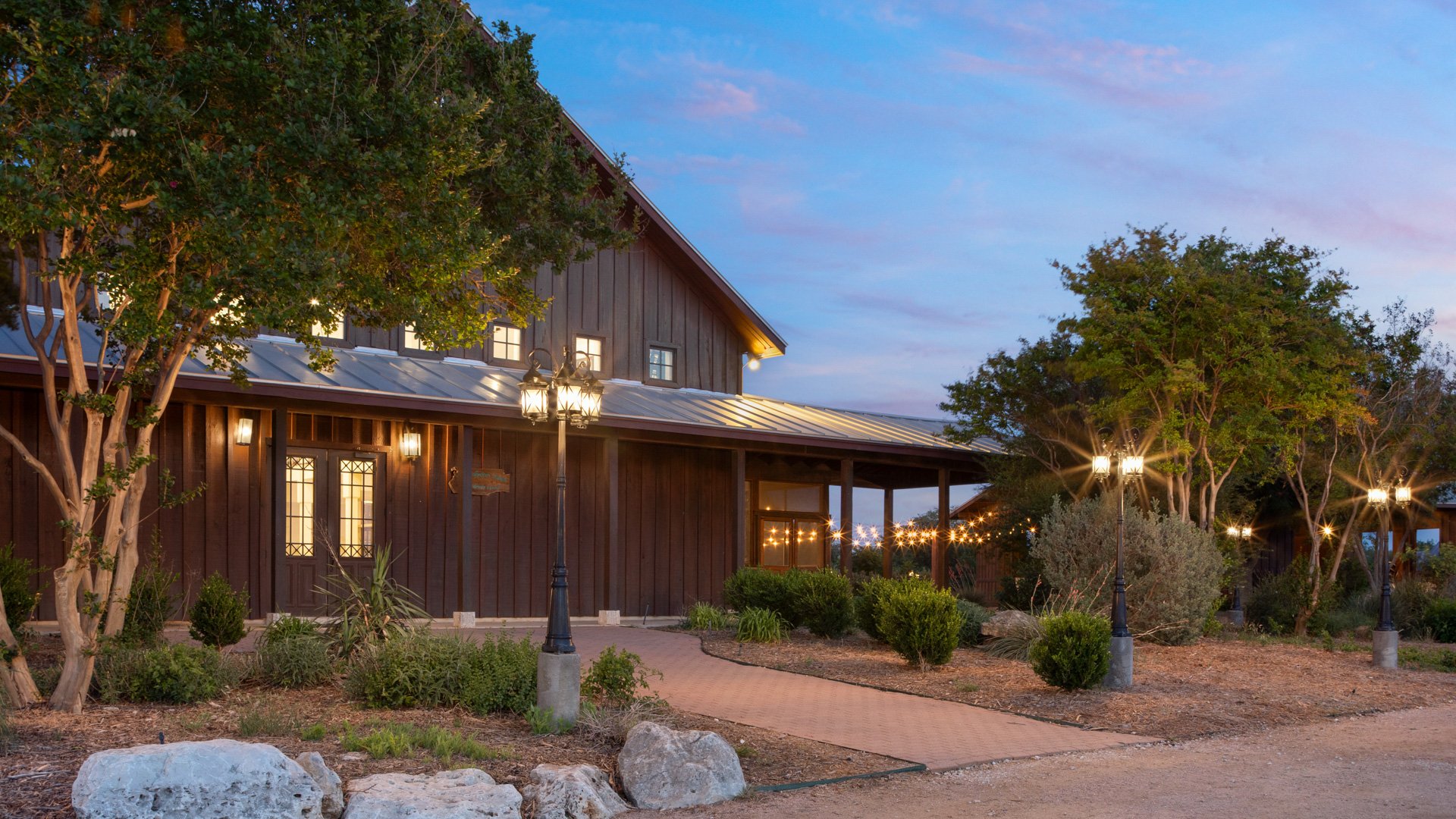 Exterior view of Hofmann Ranch barn at dusk with glowing lanterns, string lights, and landscaped pathways.