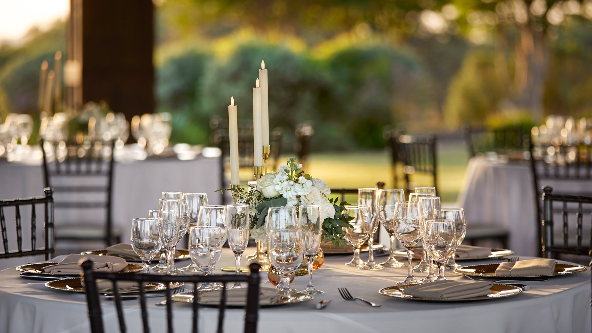 Elegant reception table at Hofmann Ranch Meadow Pavilion with white linens, tall taper candles, and sunset views of the Texas countryside.