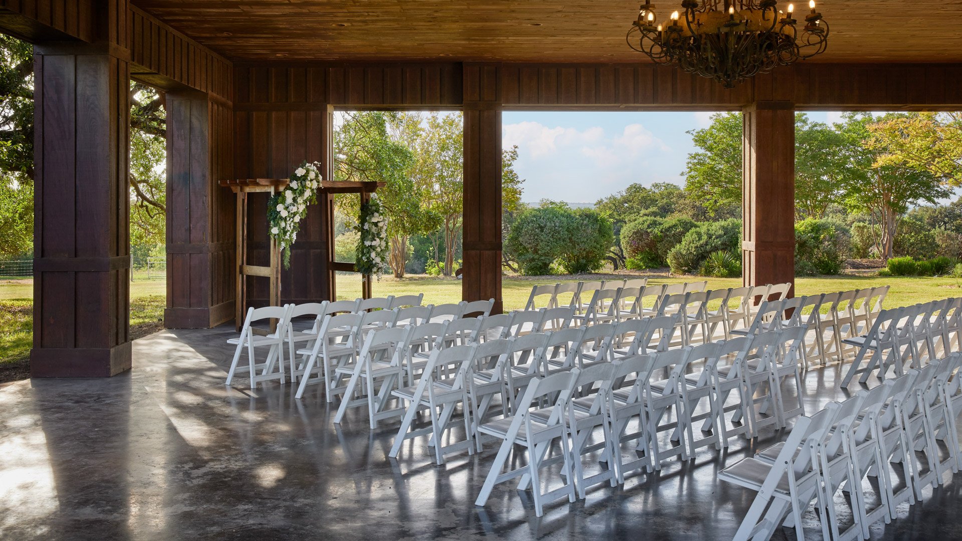 Wedding ceremony setup inside the Meadow Pavilion at Hofmann Ranch with rows of white chairs, a floral arch, and rustic wood beams framing the open-air space.