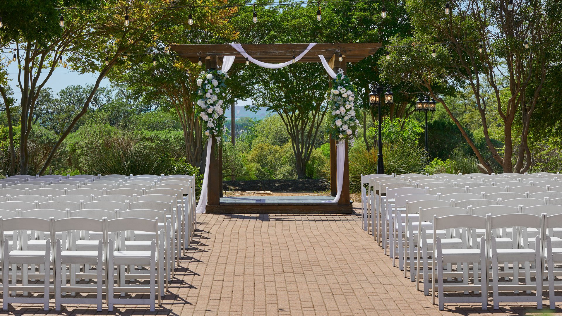 Close-up of the brick patio wedding ceremony site at Hofmann Ranch with a wooden pergola draped in white fabric and decorated with white floral arrangements.