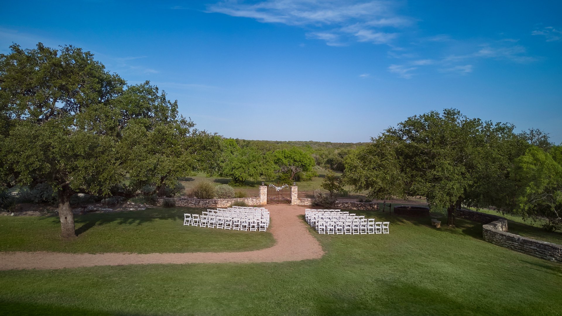 Overhead aerial view of the Iron Gate wedding ceremony site at Hofmann Ranch, with white chairs arranged outdoors and sweeping views of the Texas countryside.