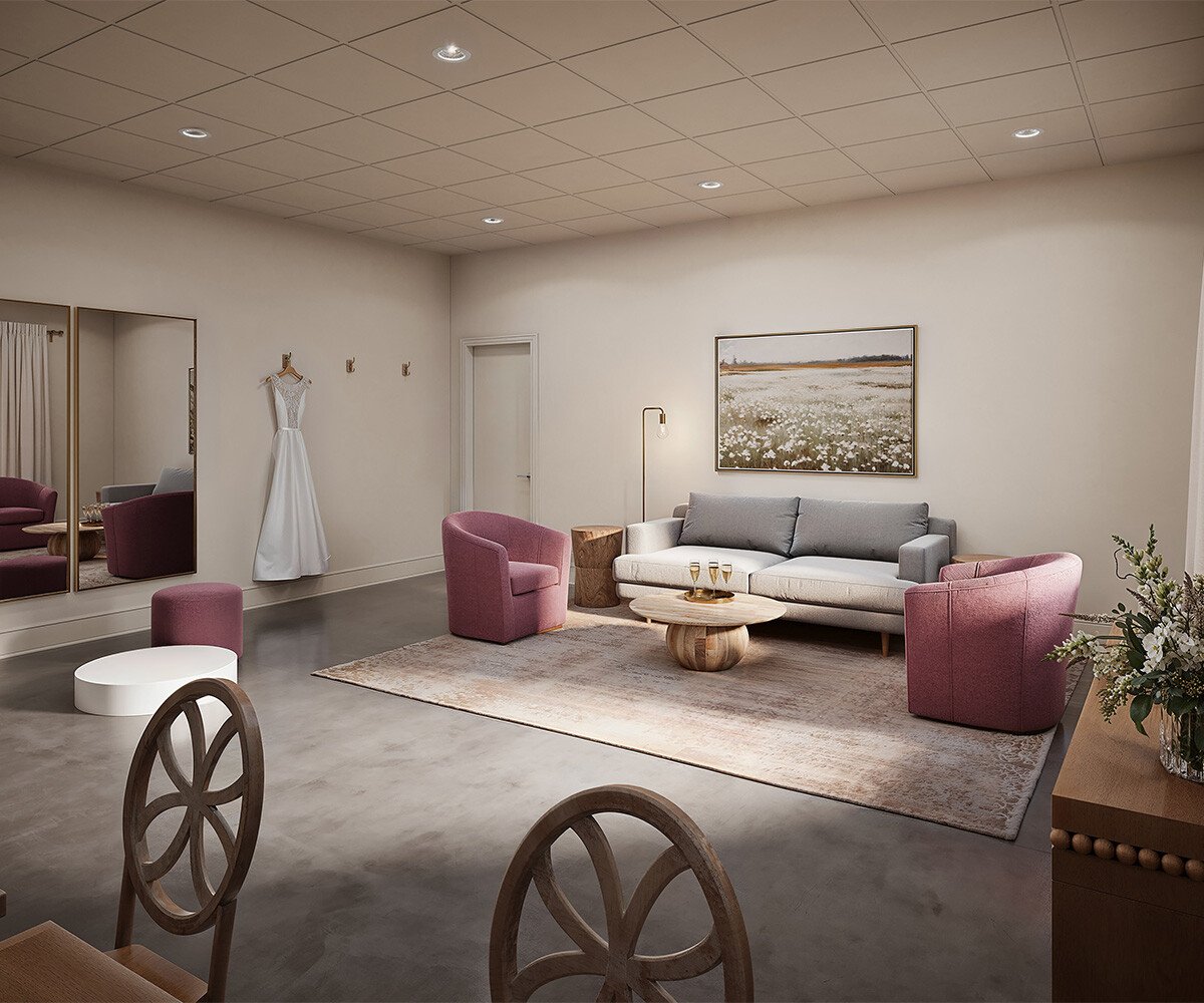 A bridal suite featuring a gray sofa, pink accent chairs, a wedding dress display, and elegant decor.