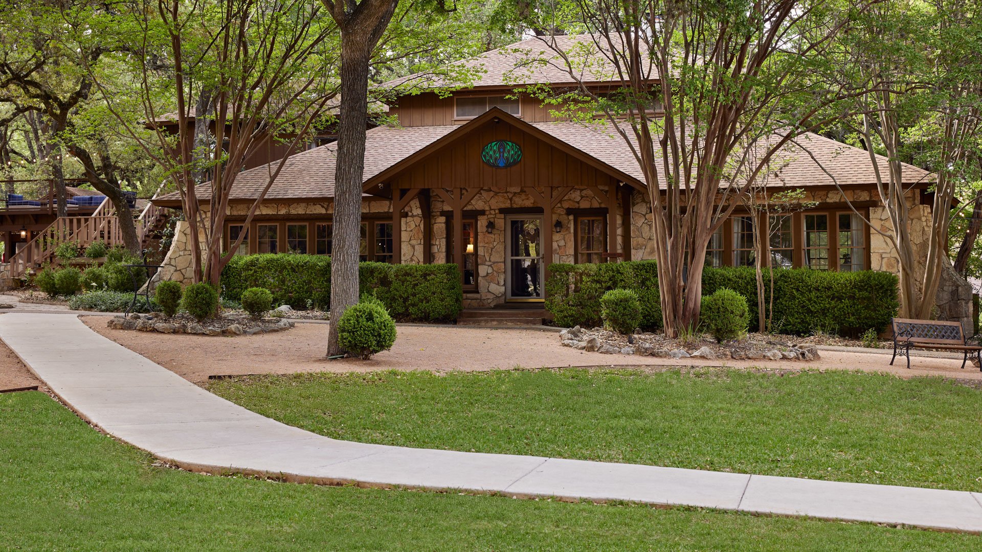 Scenic Springs stone and wood lodge-style wedding venue exterior in Helotes, Texas, surrounded by lush greenery and trees.