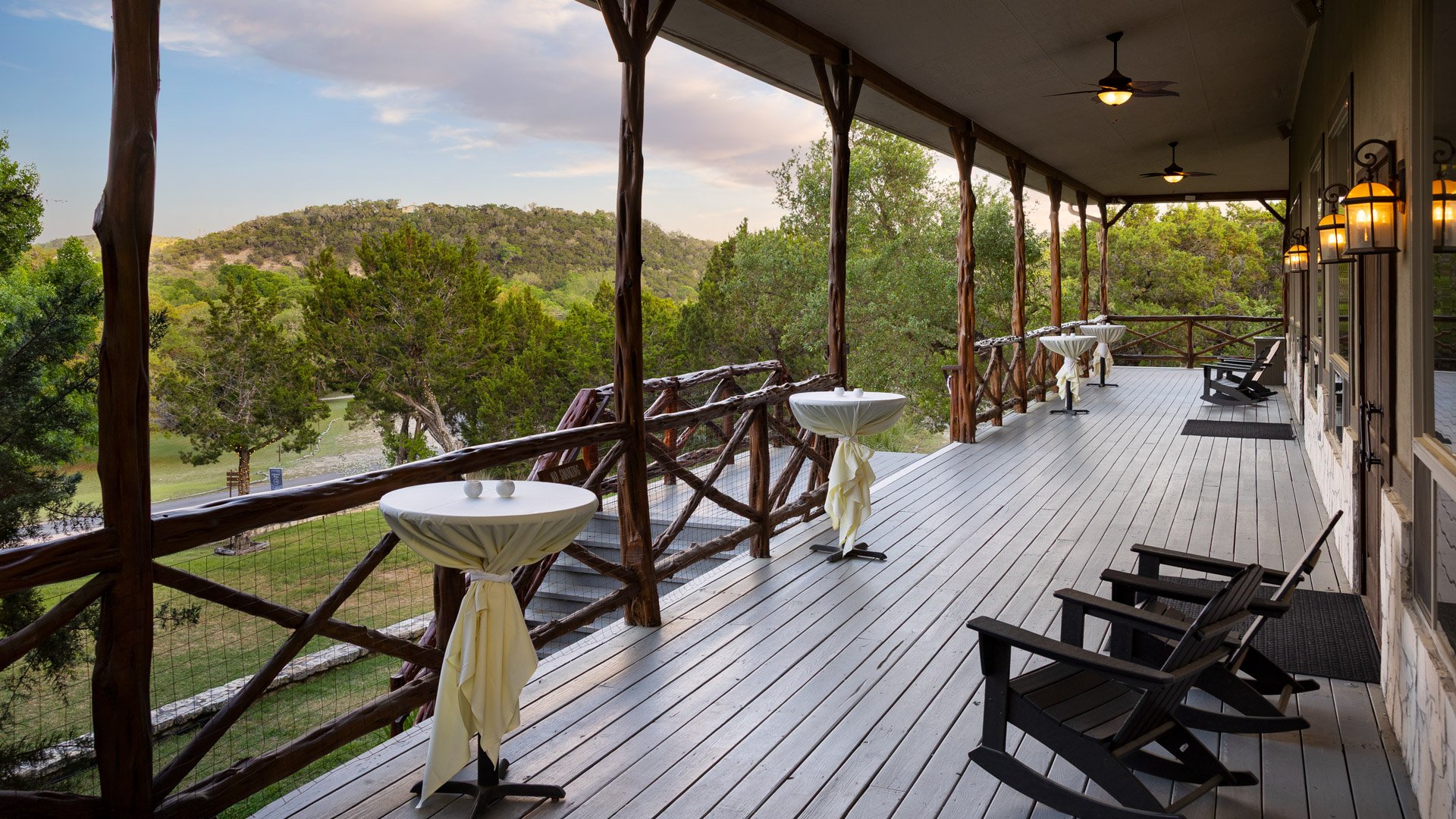 Scenic Springs porch in Helotes, Texas, set for cocktail hour with high-top tables, rocking chairs, and scenic hill country views.