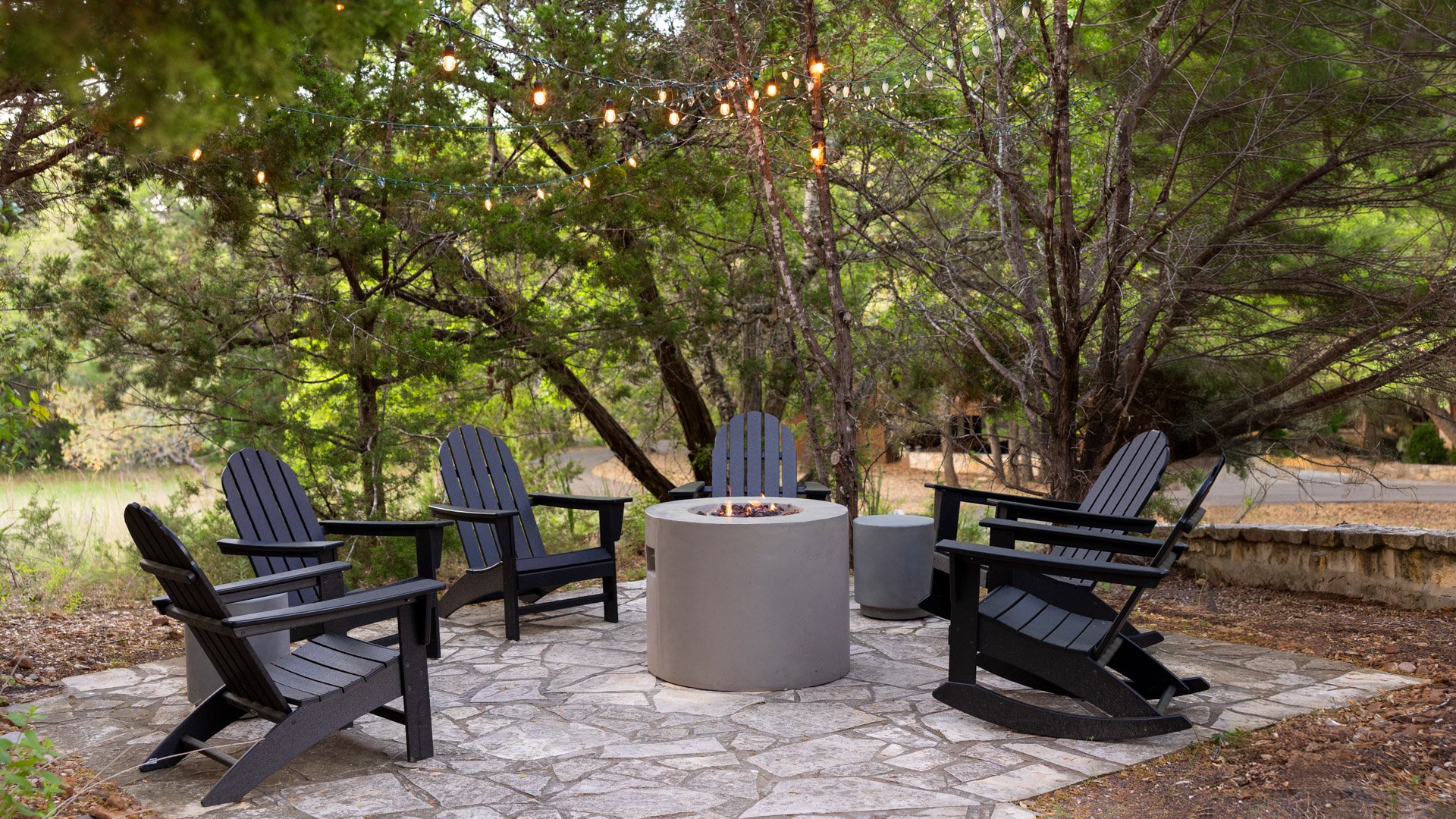 Scenic Springs outdoor firepit area in Helotes, Texas, with black Adirondack chairs and string lights under the trees.