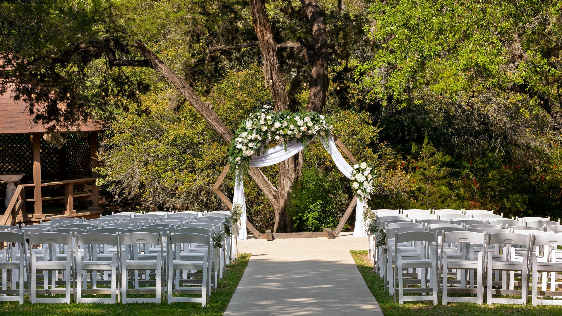 Close-up of Scenic Springs wedding ceremony setup in Helotes, Texas, with a wooden hexagon arch draped in white fabric and greenery.