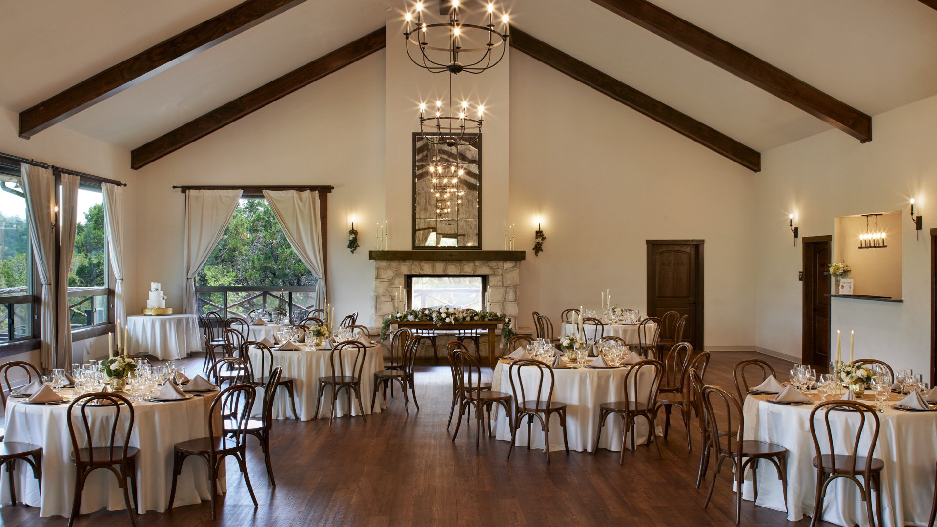 Scenic Springs ballroom wedding reception in Helotes, Texas, featuring a stone fireplace, floral décor, and round banquet tables.