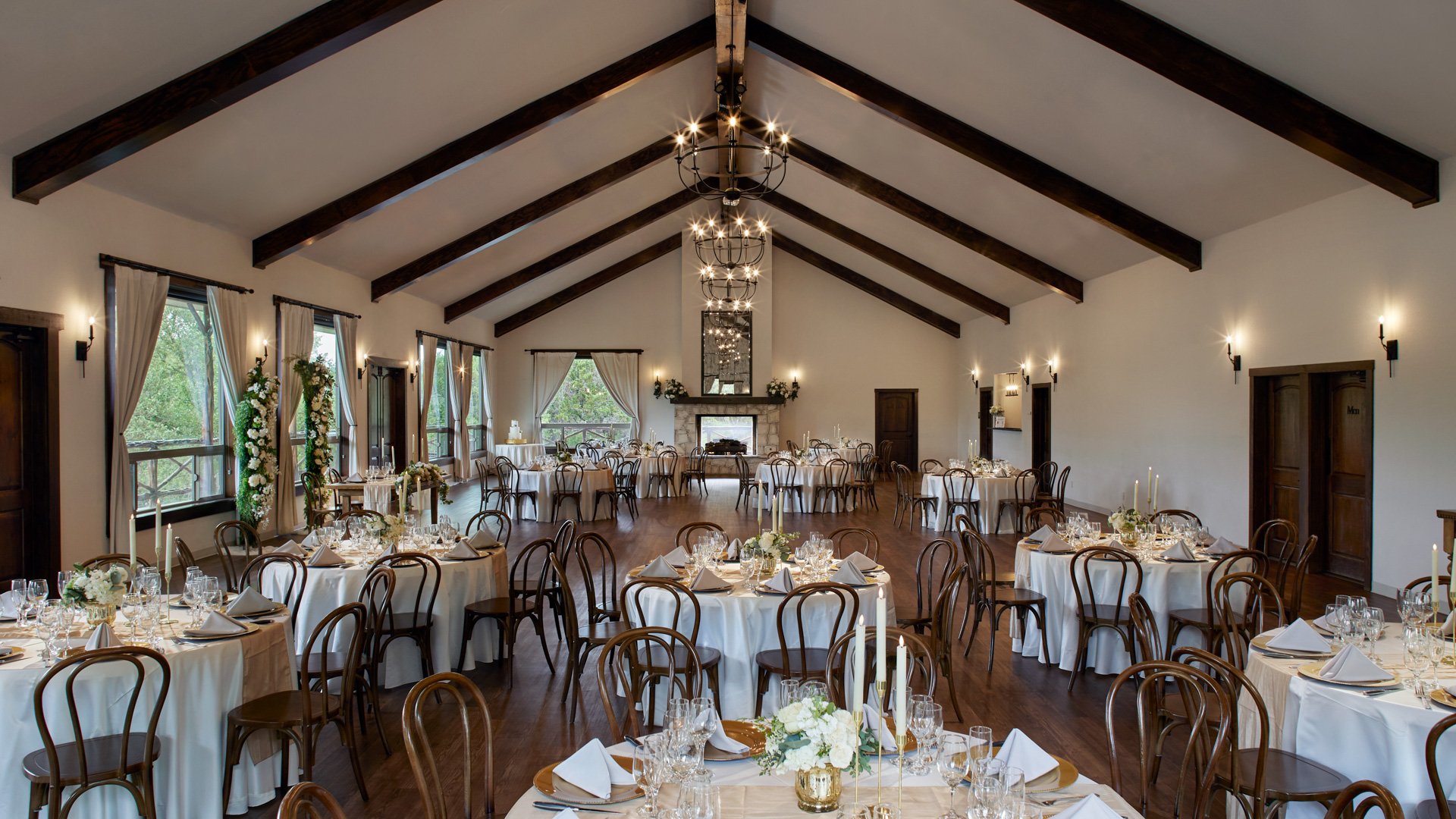 Scenic Springs Grand Ballroom wedding reception in Helotes, TX, with round tables, floral centerpieces, and rustic wood beam ceiling.