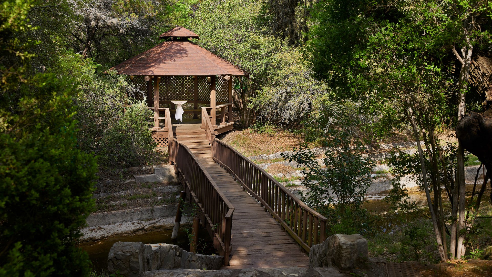Scenic Springs outdoor forest lawn wedding ceremony in Helotes, Texas, with floral arch and gazebo backdrop.