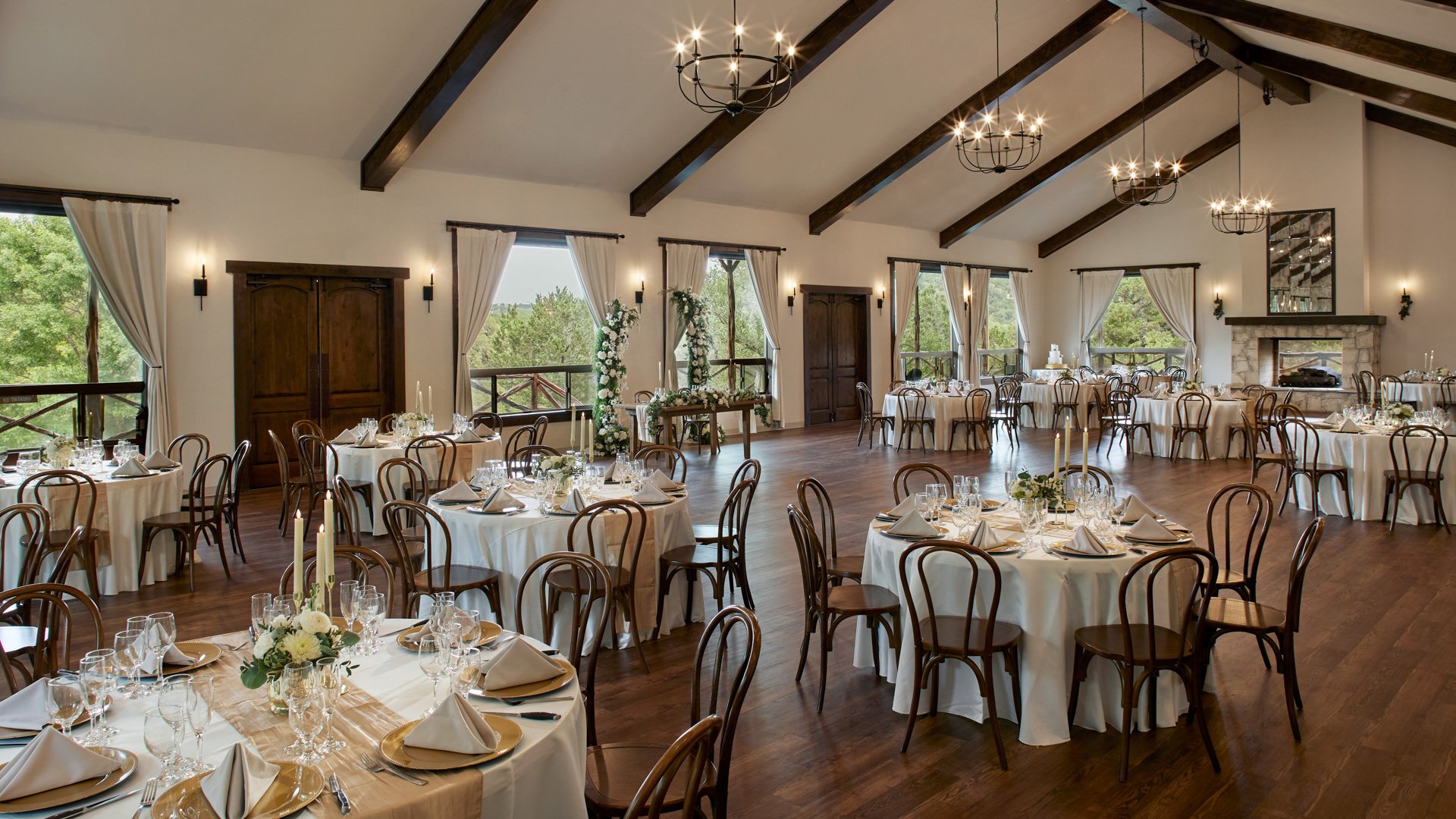 Scenic Springs Grand Ballroom in Helotes, TX, set for a wedding with decorated tables, rustic chandeliers, and a stone fireplace.