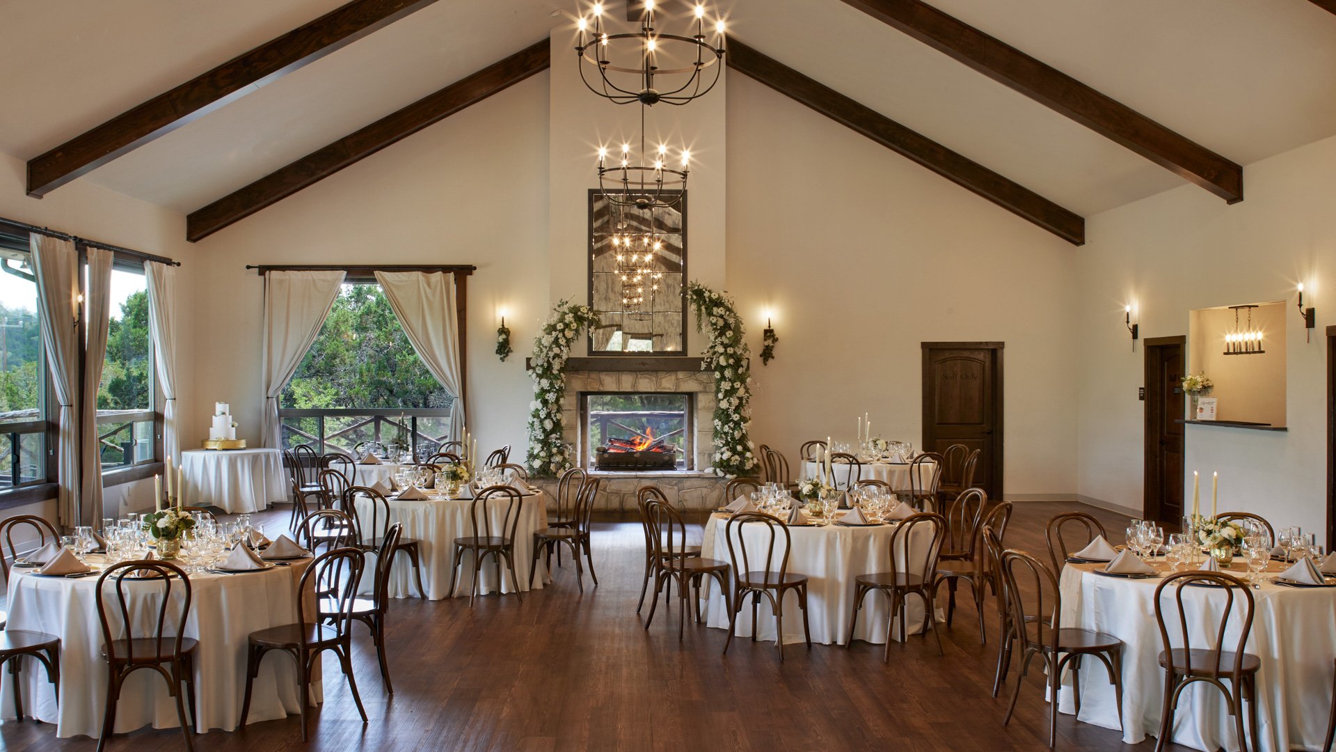 Scenic Springs reception hall decorated for a wedding with floral arch at the fireplace, banquet tables, and elegant chandeliers.