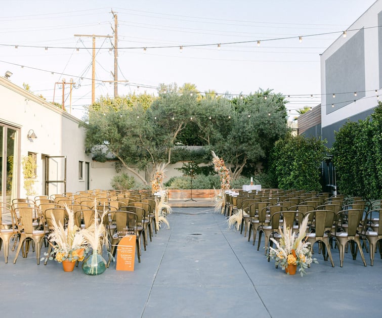 Boho courtyard ceremony space at The Harper Costa Mesa featuring pampas grass arrangements, gold metal chairs and string lights