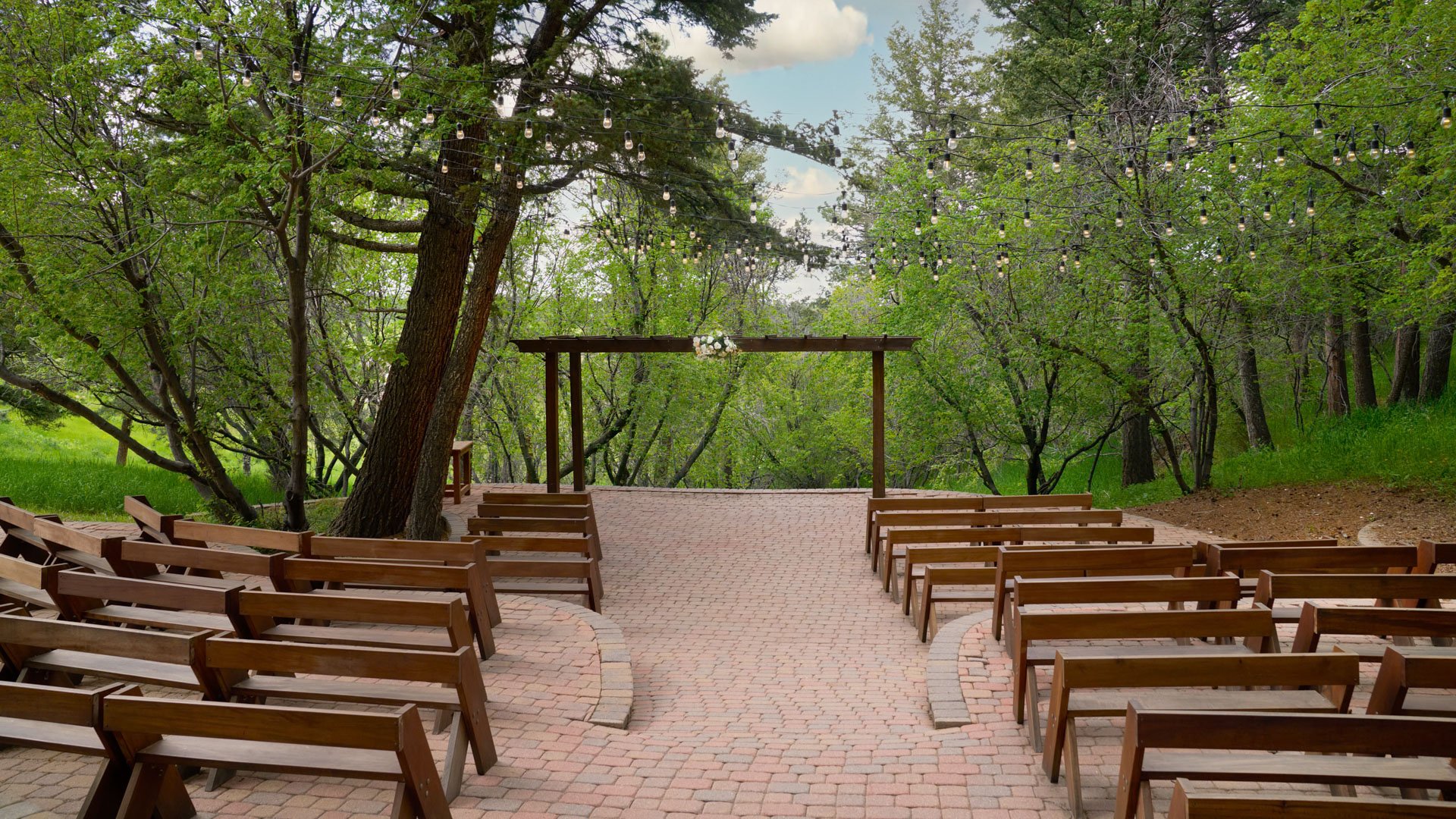 Outdoor wedding ceremony setup at The Pines’ Aspen Terrace in Colorado featuring wooden benches, a rustic arch, and string lights surrounded by lush forest scenery.