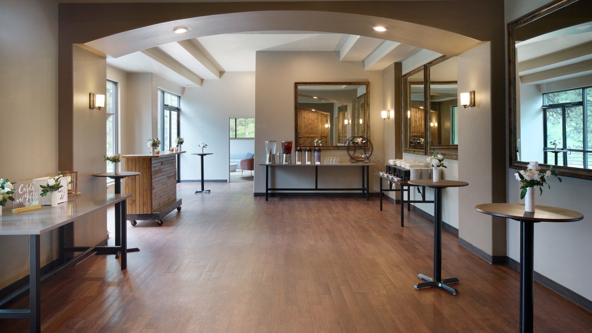 Stylish cocktail lounge at The Pines with wood flooring, mirrors, tall tables with white flowers, and natural light pouring through large windows.