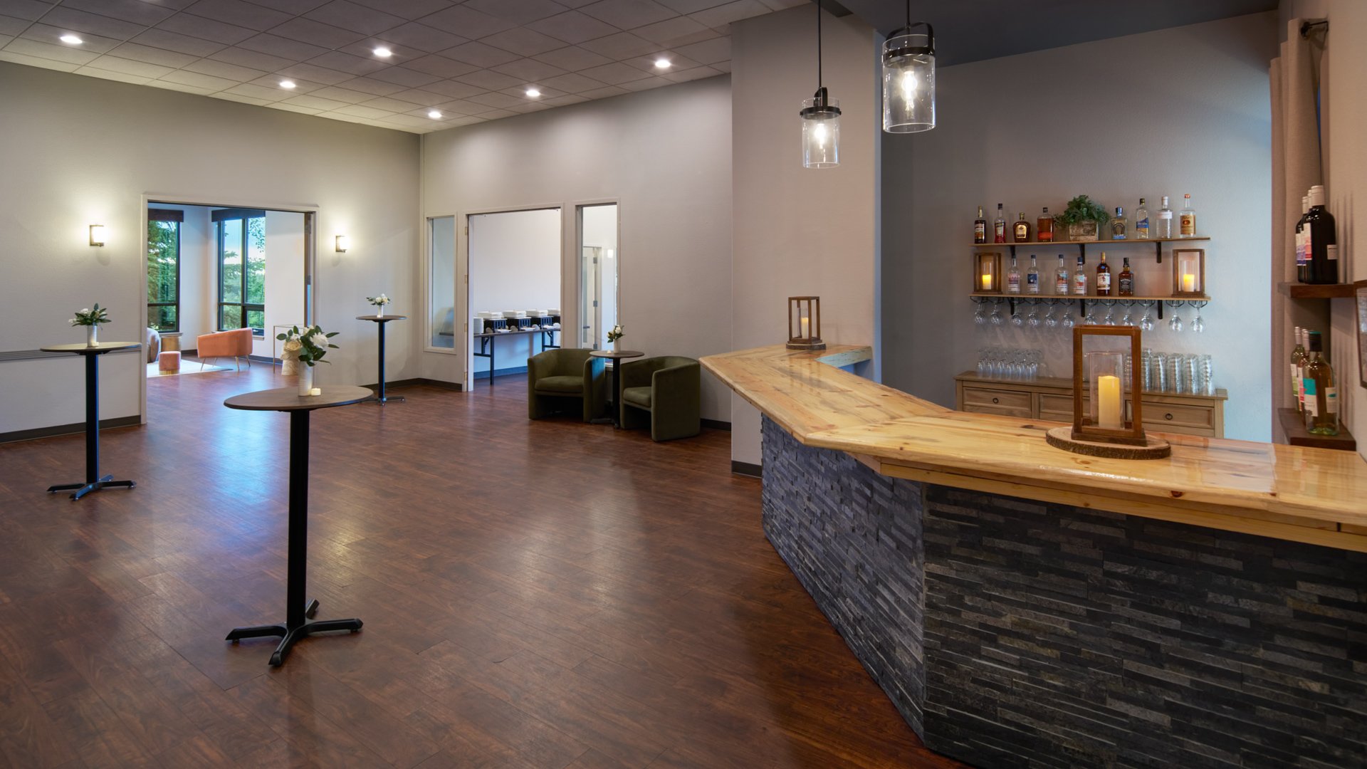 Modern rustic cocktail bar area at The Pines with wooden countertop, hanging pendant lights, and tall tables decorated with floral centerpieces.