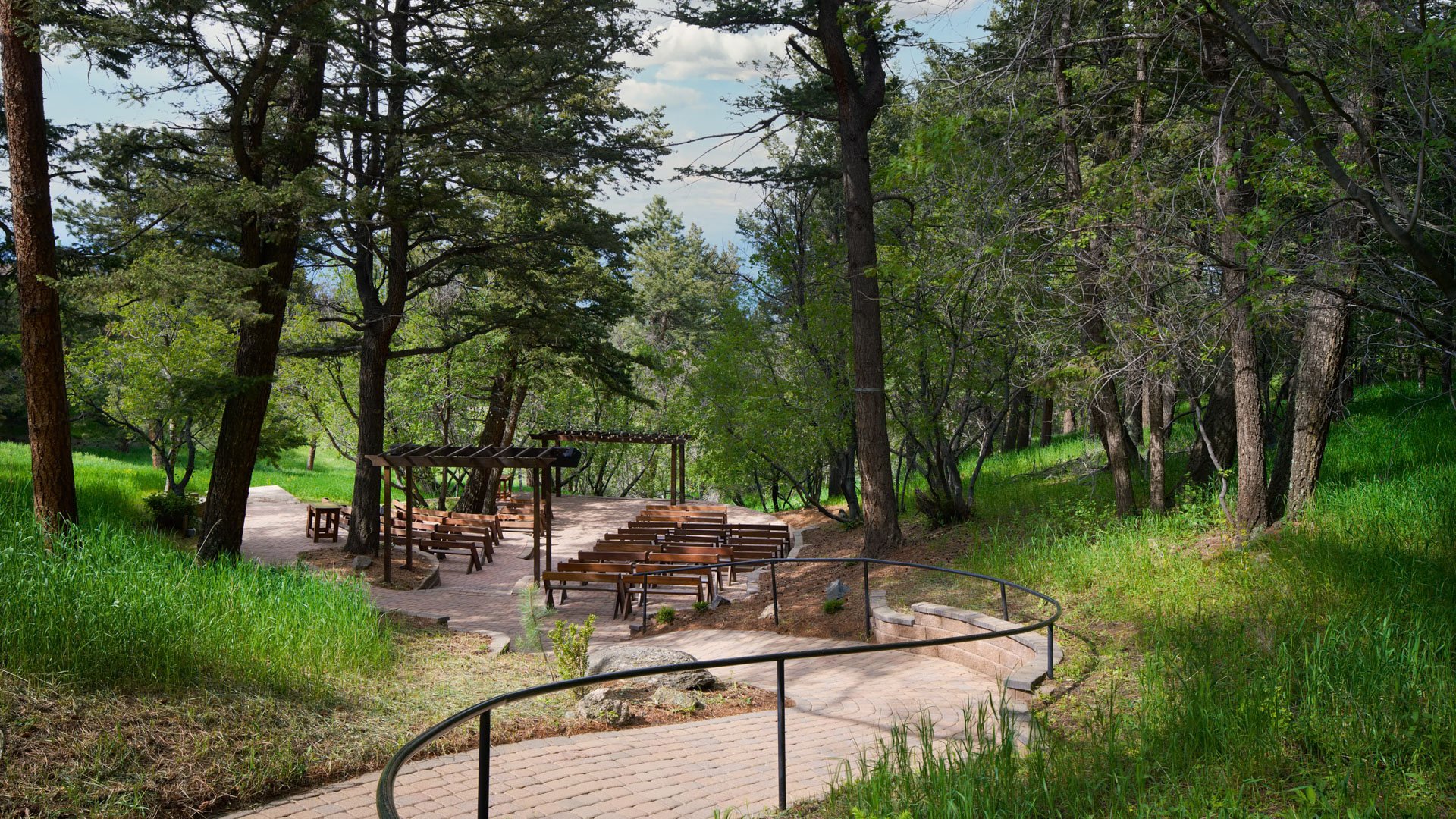 Woodland wedding ceremony setup at The Pines Aspen Terrace featuring wooden benches, a rustic pergola, and a stone pathway surrounded by tall pine trees.