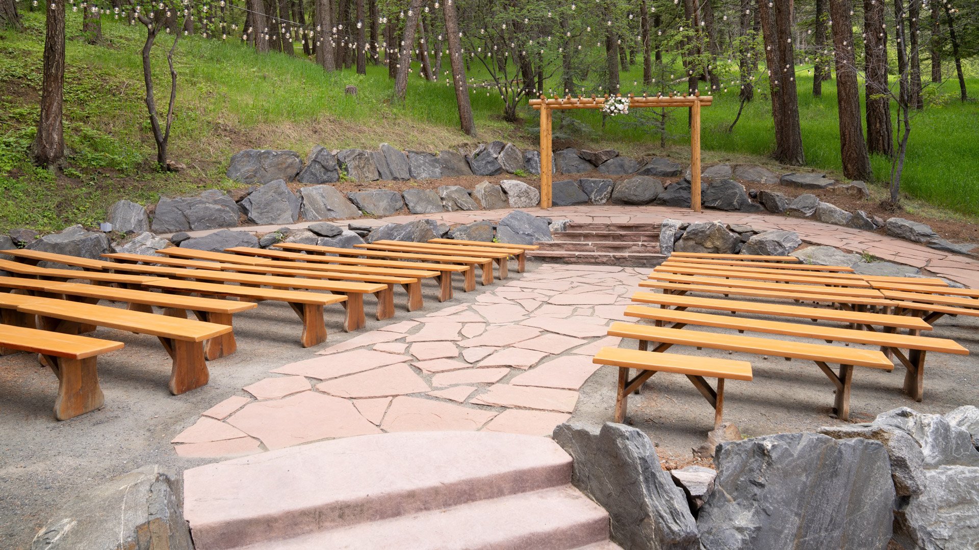 Outdoor ceremony site at The Pines’ Evergreen Terrace featuring natural stone pathways, wooden benches, and a timber arch framed by forest trees.