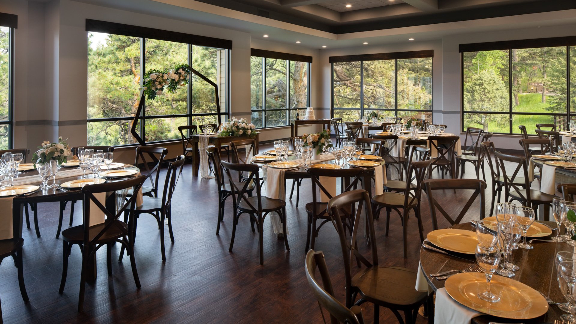 Elegant indoor wedding reception at The Pines with round wooden tables, floral centerpieces, and scenic forest views through large windows.