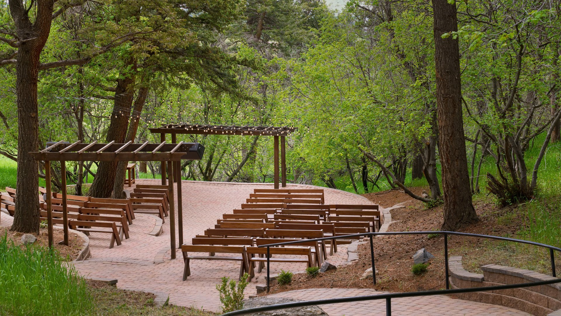 Wide-angle view of The Pines Aspen Terrace ceremony space featuring rustic wooden seating, twinkle lights, and towering pine trees.