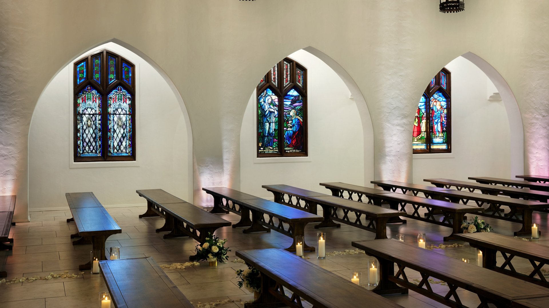 Wedding ceremony aisle at The Sanctuary Cathedral in Long Beach with wooden benches, candles, and stained glass windows.