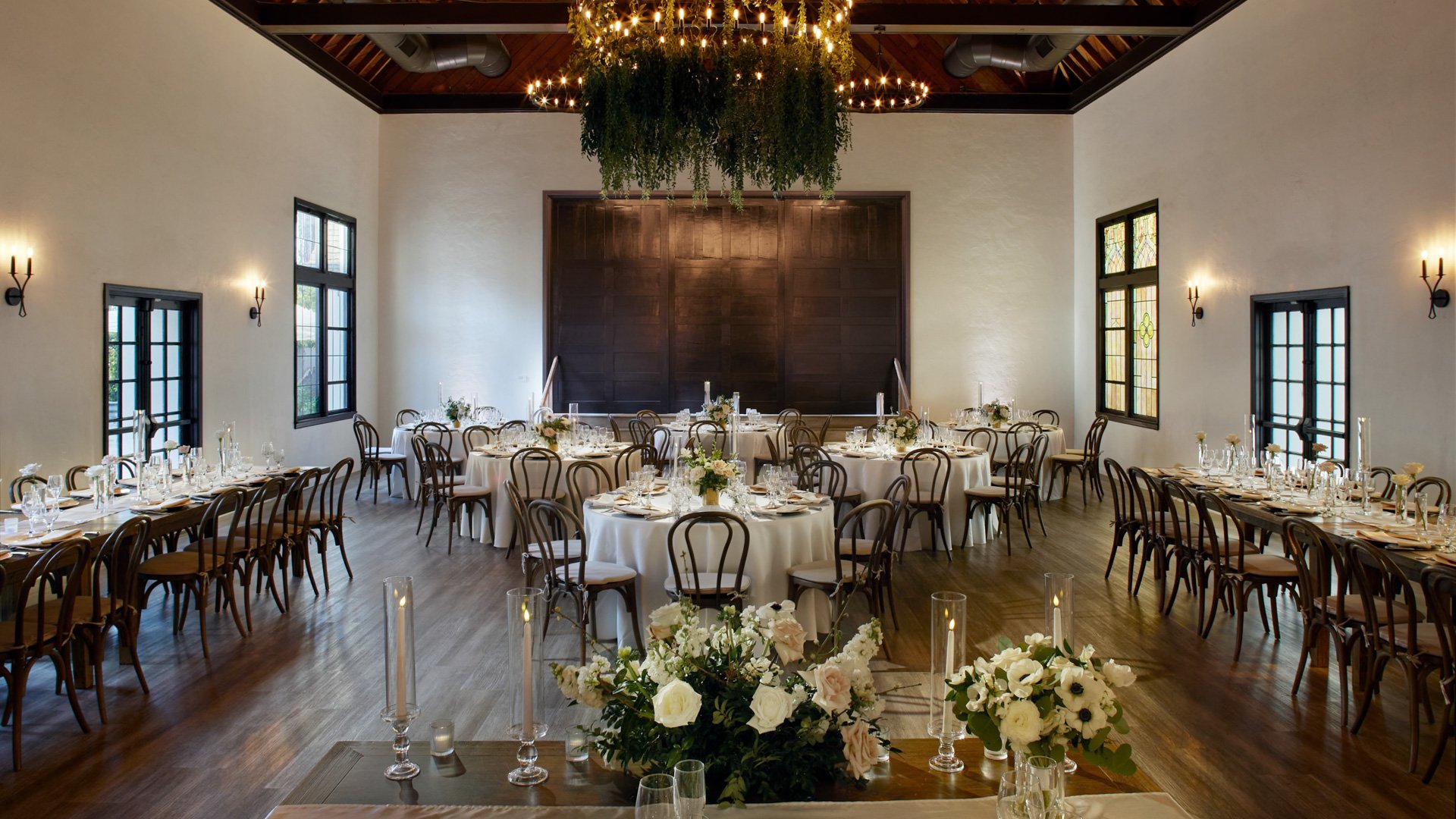 Grand Hall at The Sanctuary in Long Beach set for a wedding reception with round and long tables under a greenery chandelier.