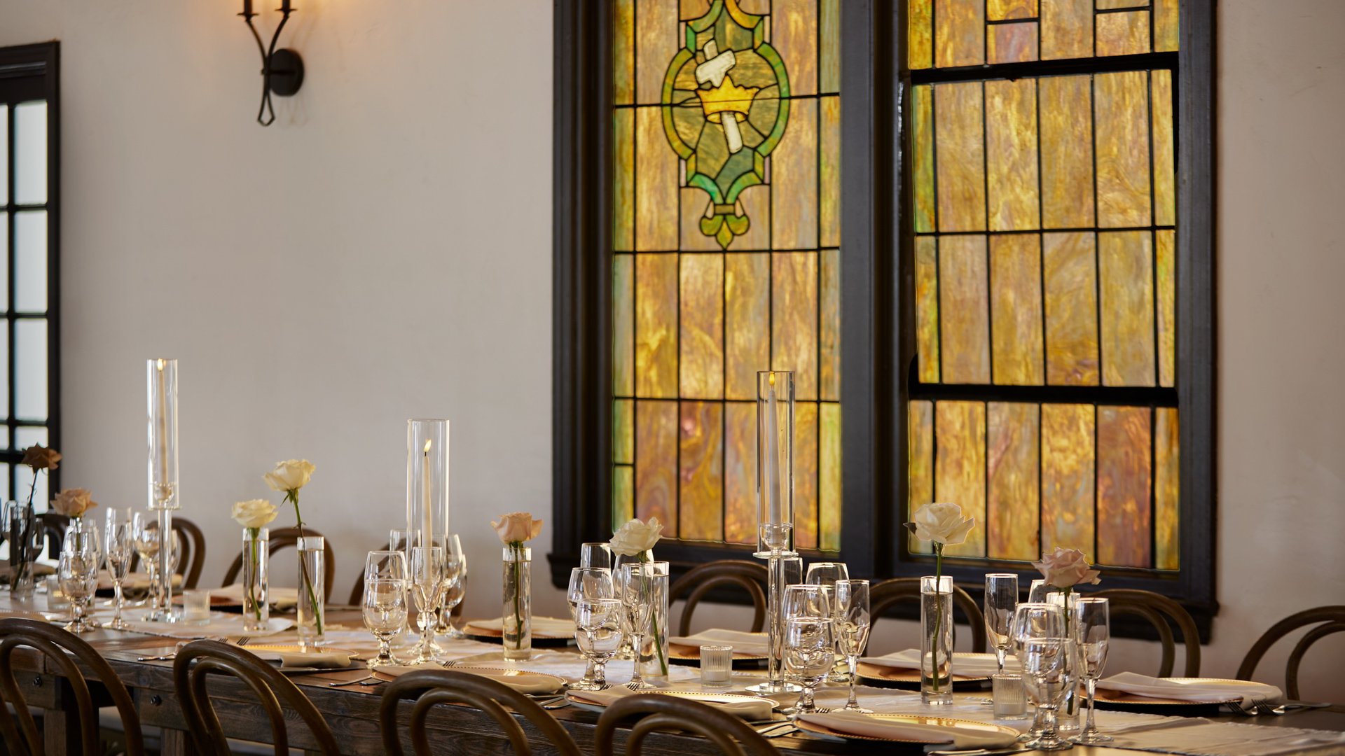 Elegant wedding table setting at The Sanctuary Grand Hall in Long Beach with single rose centerpieces and stained glass backdrop.