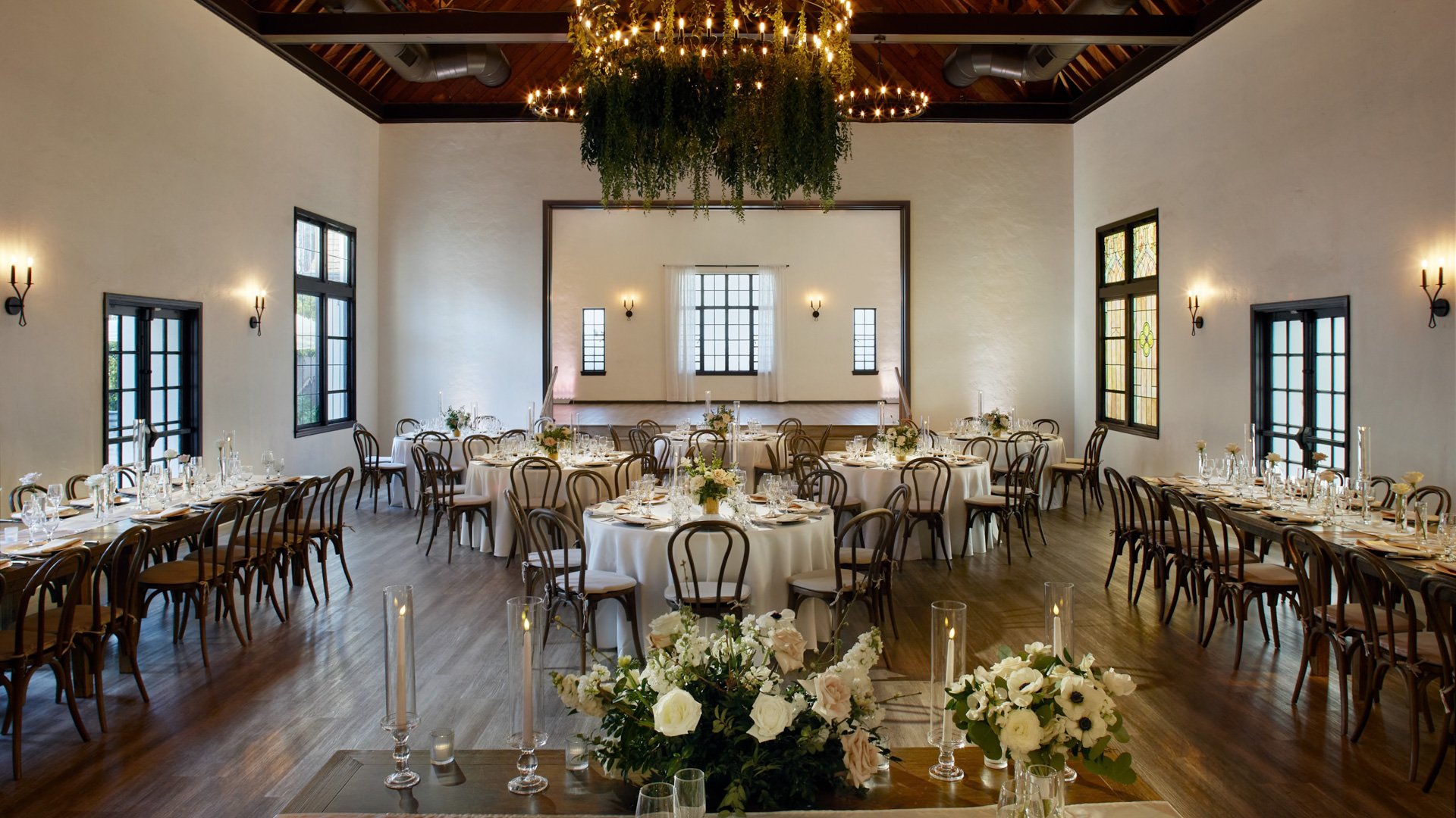 The Grand Hall at The Sanctuary in Long Beach set for a wedding reception with round tables, greenery chandelier, and white florals.