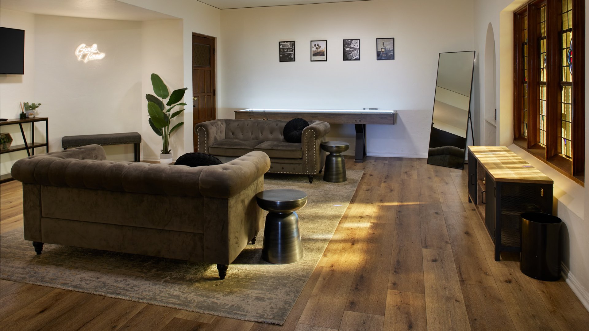 Groom’s lounge suite at The Sanctuary in Long Beach with tufted sofas, shuffleboard table, and warm stained glass windows.