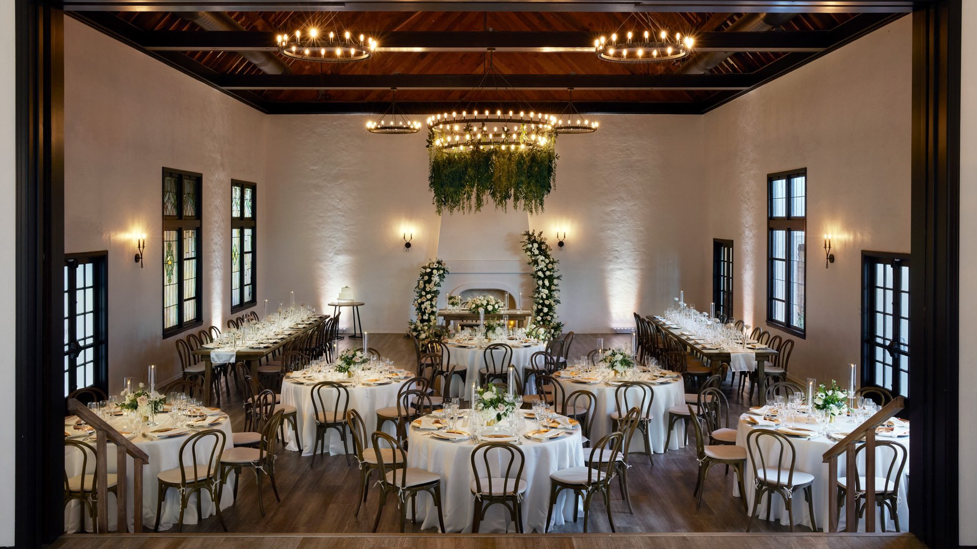 Wide view of The Sanctuary Grand Hall wedding reception in Long Beach with chandelier greenery and candlelit tables.