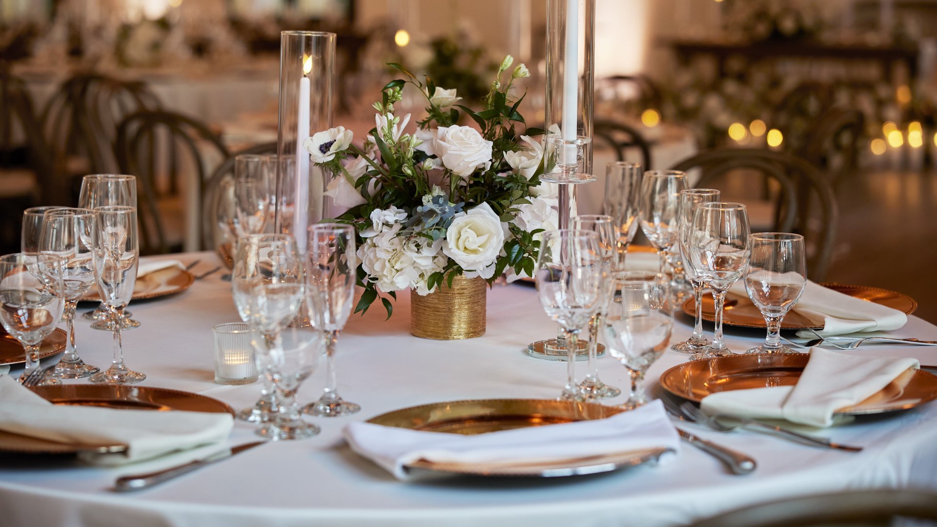 Elegant wedding reception centerpiece at The Sanctuary in Long Beach with white roses, greenery, and candlelight.