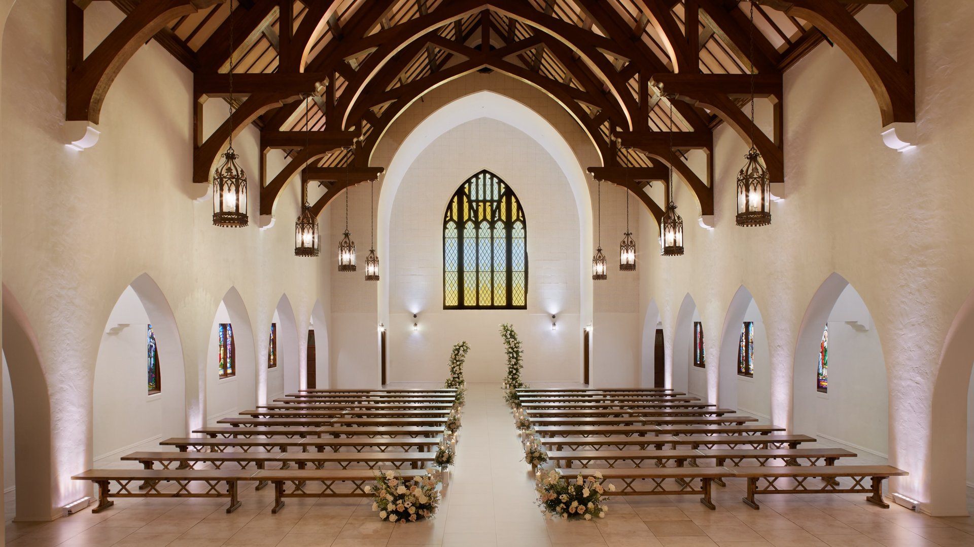 Wedding ceremony inside The Sanctuary Cathedral in Long Beach featuring a stained-glass window backdrop and romantic floral décor.