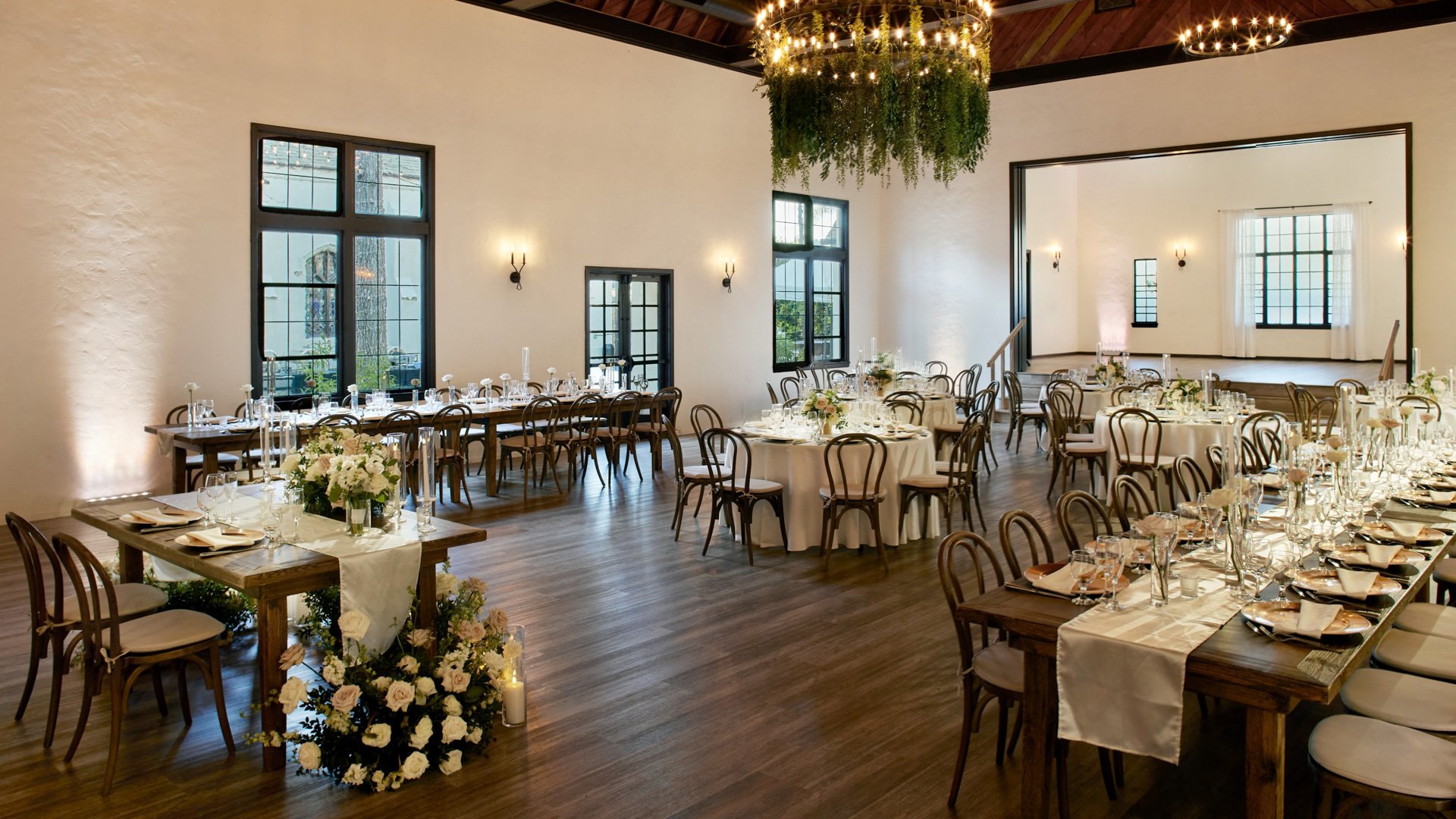 Grand Hall at The Sanctuary, Long Beach, arranged for a wedding reception with long and round tables, candlelight, and greenery chandelier.
