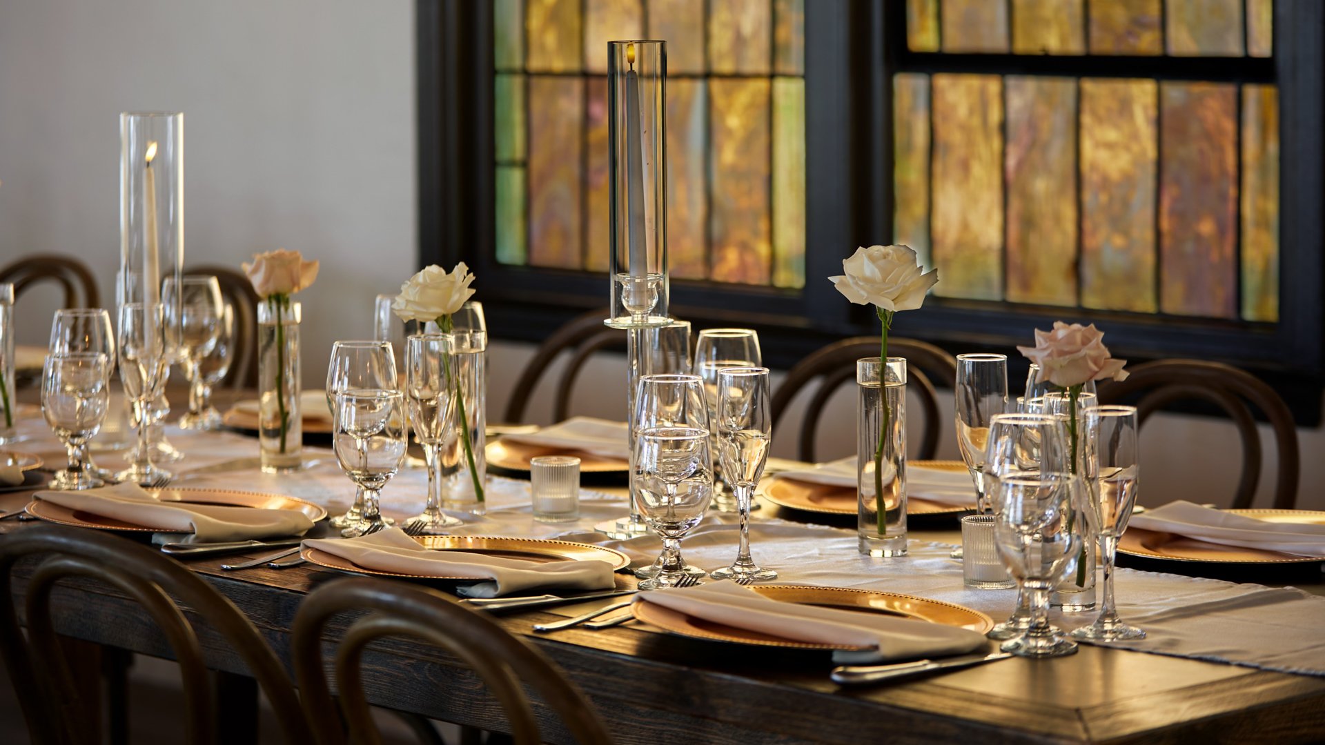 Elegant wedding table setting in The Sanctuary’s Grand Hall, Long Beach, with gold chargers, glassware, and single rose centerpieces.