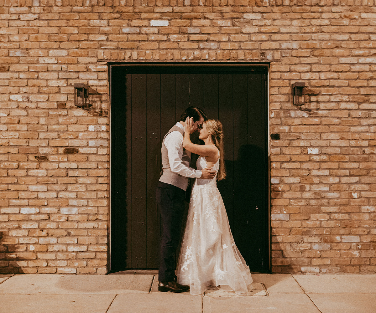 Couple posing in front of brick wall & doors - Tre Bella by Wedgewood Weddings