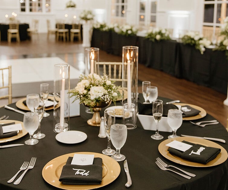 Elegant black and gold wedding tablescape featuring floral centerpieces, tall candles, and personalized napkins at Lindsay Grove.