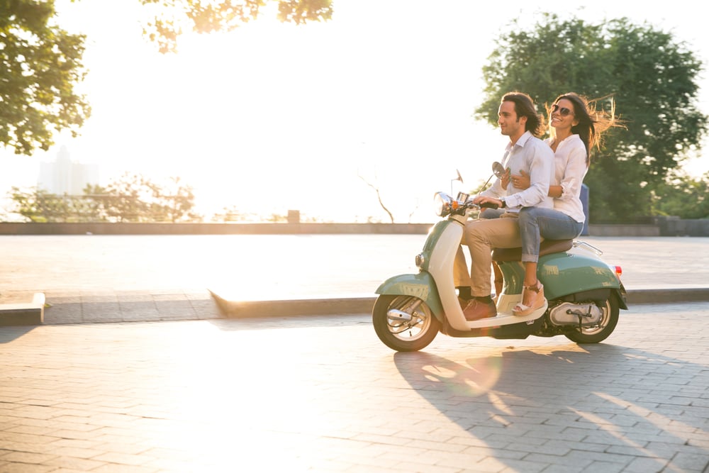 Happy young couple riding a scooter and having fun. Sun is shining in the morning