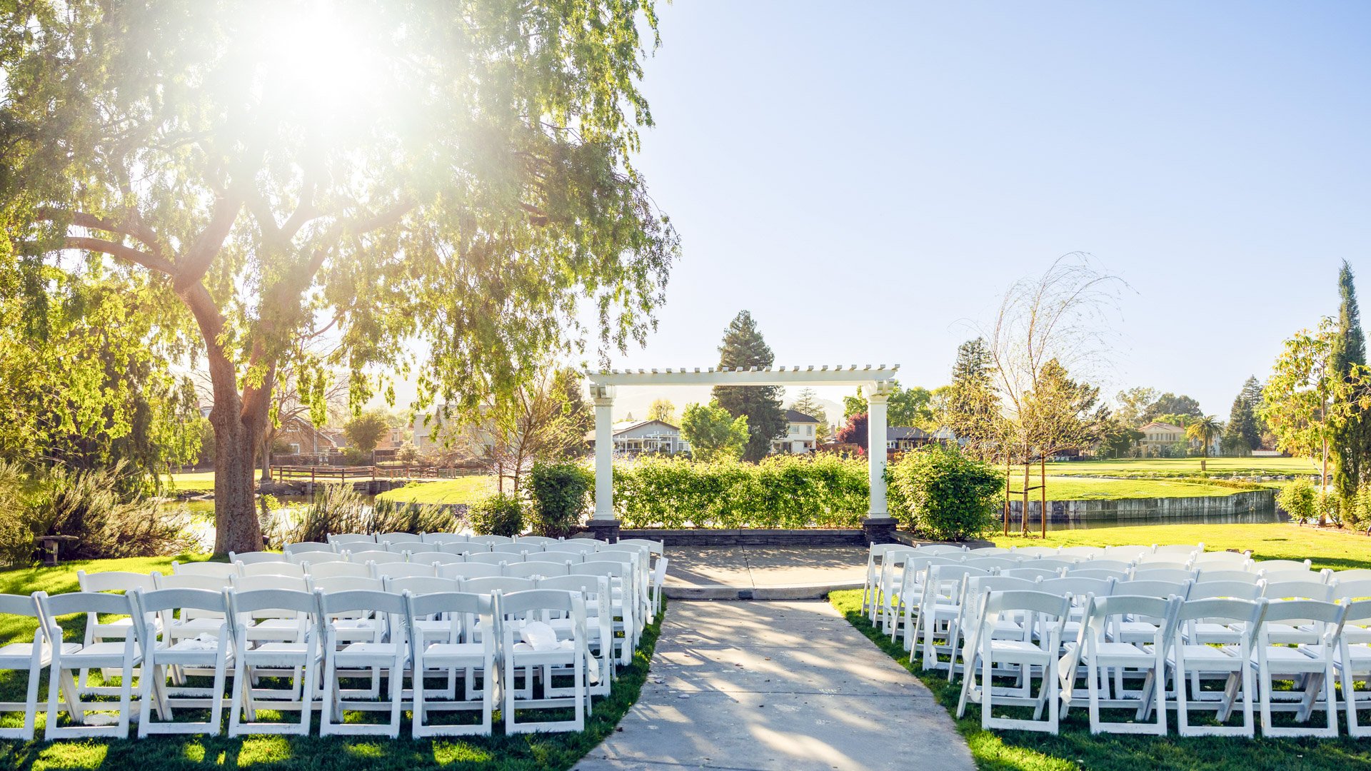 Outdoor Garden Wedding Ceremony Site with White Draped Pergola and Willow Tree Backdrop
