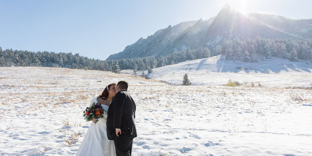 Bride and groom kissing in snow in front of Boulder mountains - Boulder Creek by Wedgewood Weddings