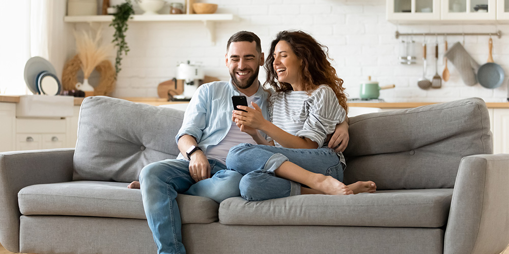 Couple on the couch, laughing while on their phone
