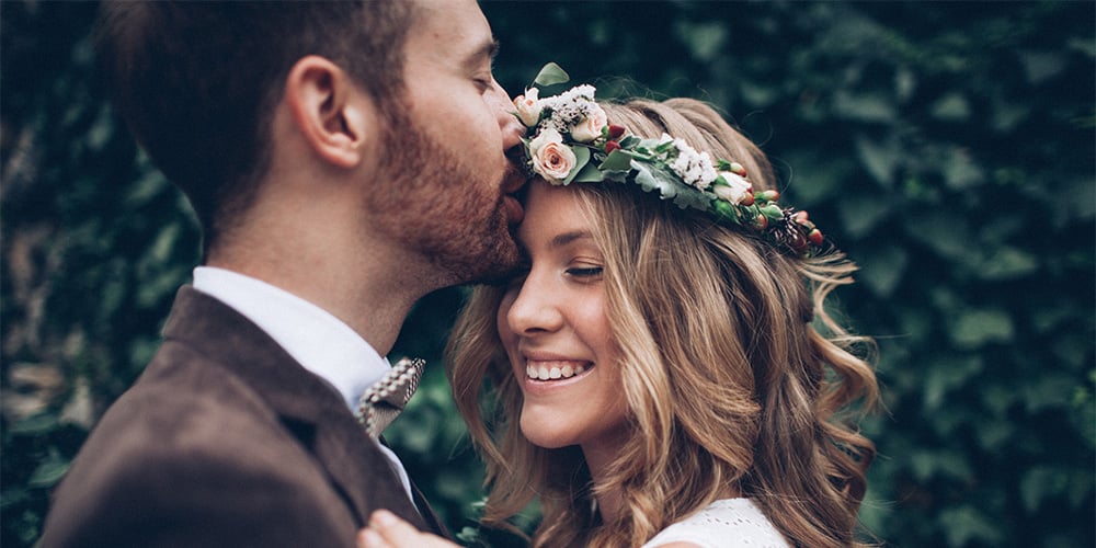Happy couple, groom kissing bride on forehead. Bride with flowers in her hair